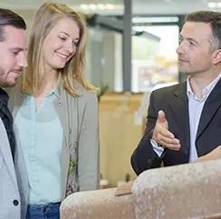 Sales representative showing a product sample to a smiling couple in a showroom.