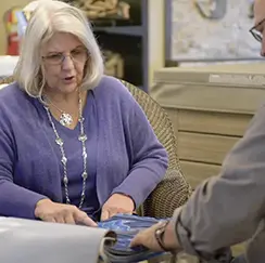 Older woman reviewing fabric samples with a customer in a showroom or design office.