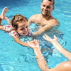 Happy family teaching a young girl to swim in a clear blue swimming pool.