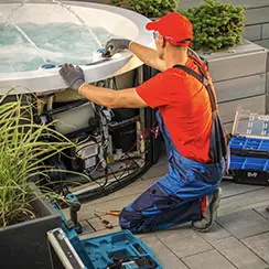 Technician in red shirt and blue overalls repairing or servicing a hot tub outdoors.