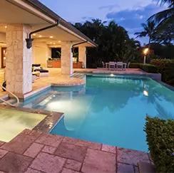 Luxury backyard with illuminated swimming pool, spa, and covered patio area at dusk.